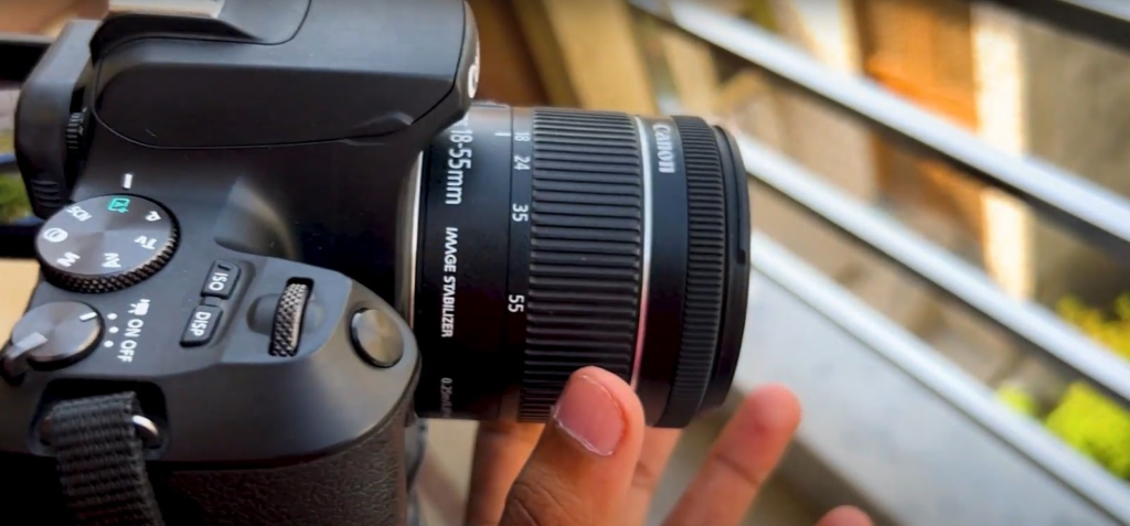 the 18-55mm Canon lens mounted on a camera with a hand adjusting it
