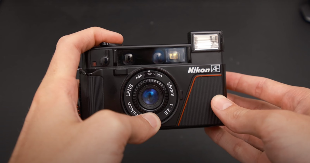 the Nikon L35AF camera in hands pressing a button showcasing the built-in flash