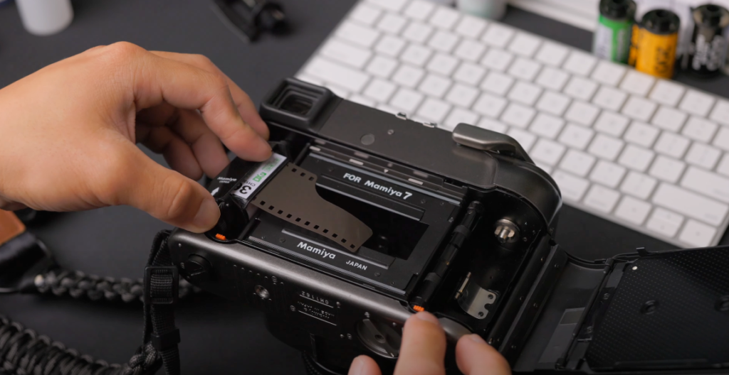 A hand inserting a film roll into a black camera.