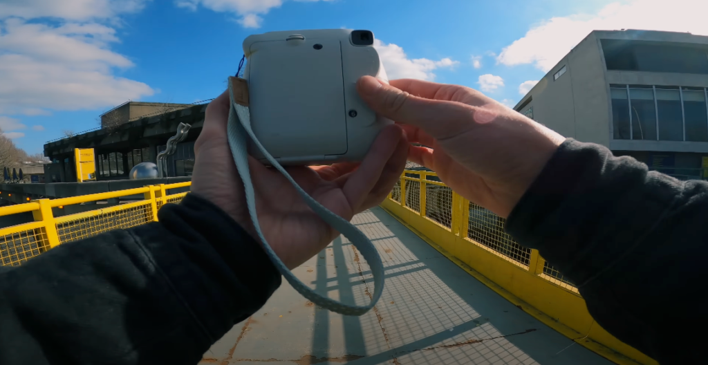 A photo of hands holding a white Instax camera, capturing the surrounding view at the bridge.