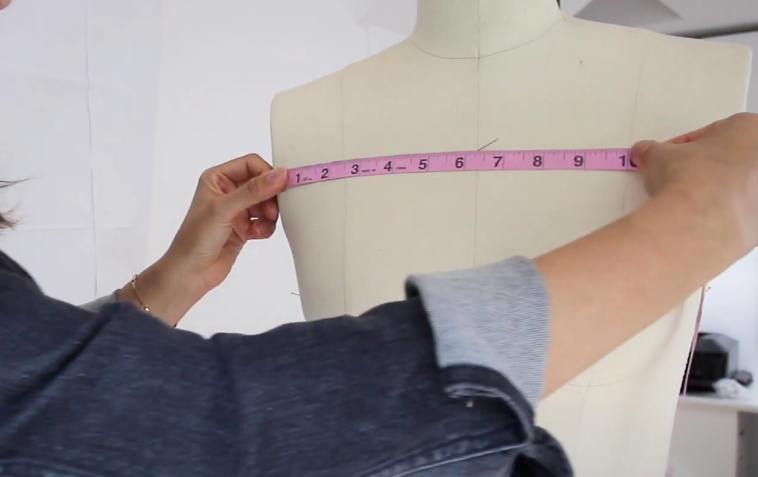 A hand measuring a mannequin using a pink measuring tape.