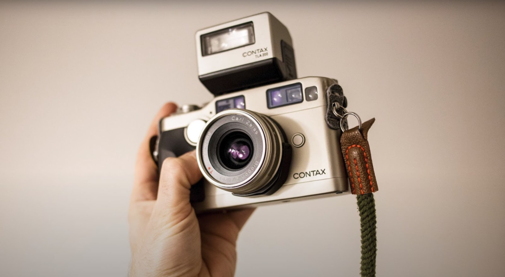 a hand holding the Contax G1 camera with a strap on a grey background