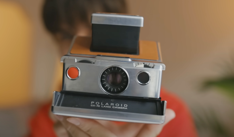 Front view of a silver, black, and mustard-colored Polaroid SX-70 camera.
