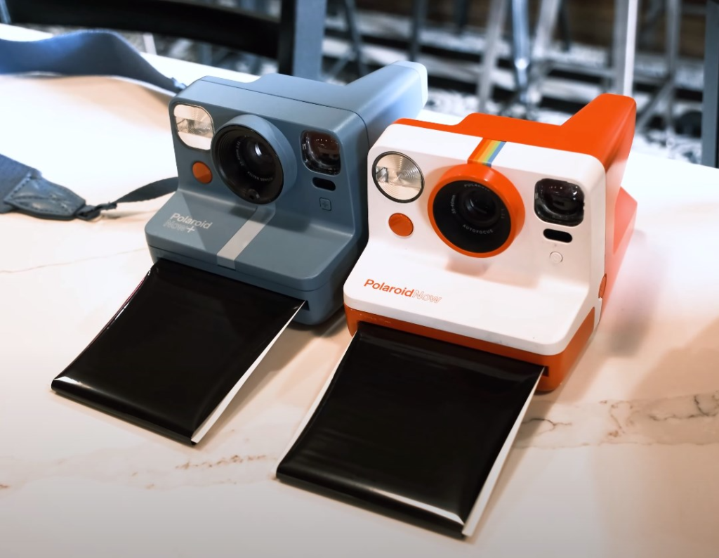 two Polaroid cams with film on a white table 