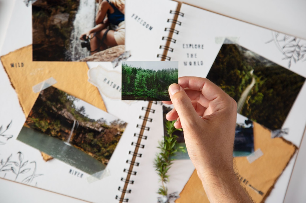 a hand holding a small picture of a forest on a background with various photos and a notebook