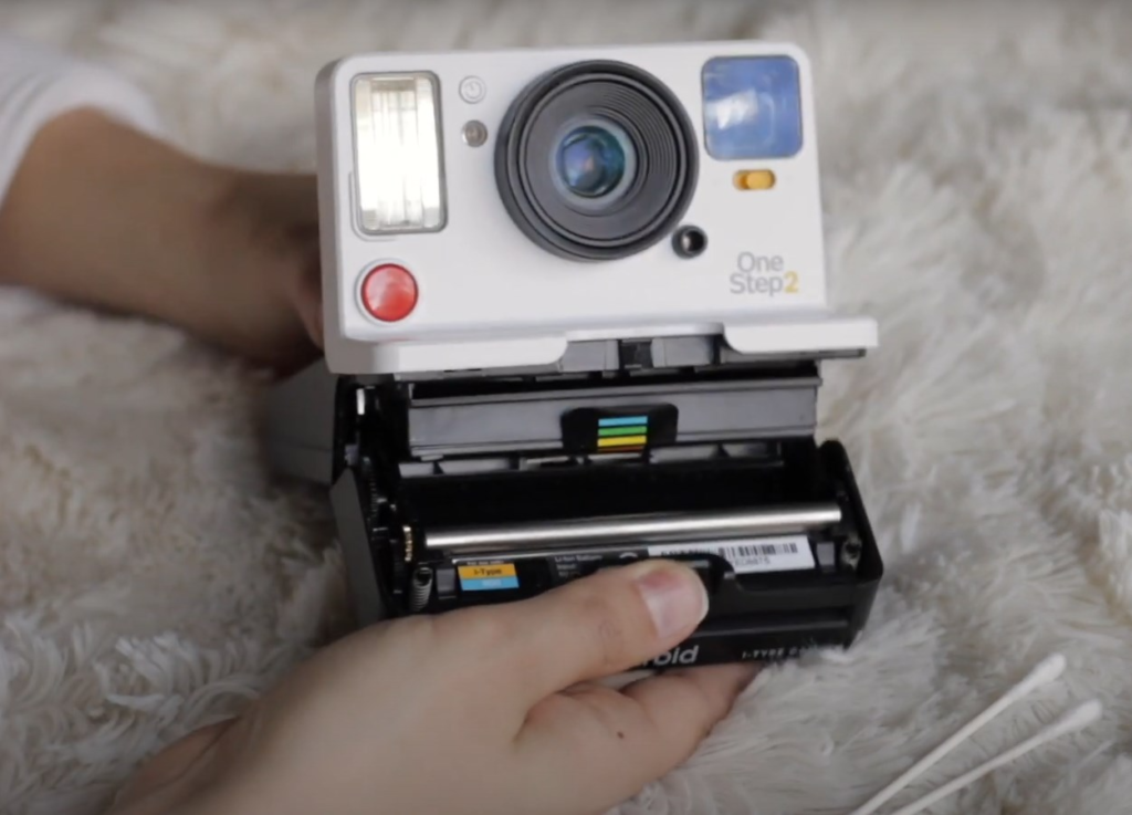 a Polaroid camera in the hands of a woman with two Q-tips on a fluffy background