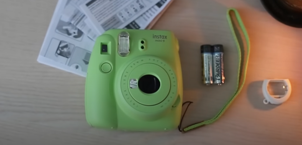 A green Instax Mini 9 camera, 2 batteries, and instructions on the wooden table