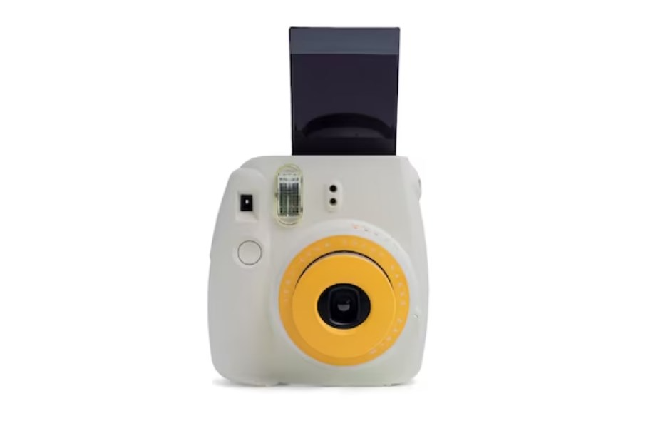 a white Instax Mini camera with a yellow lens and a sticking-out blank photo
